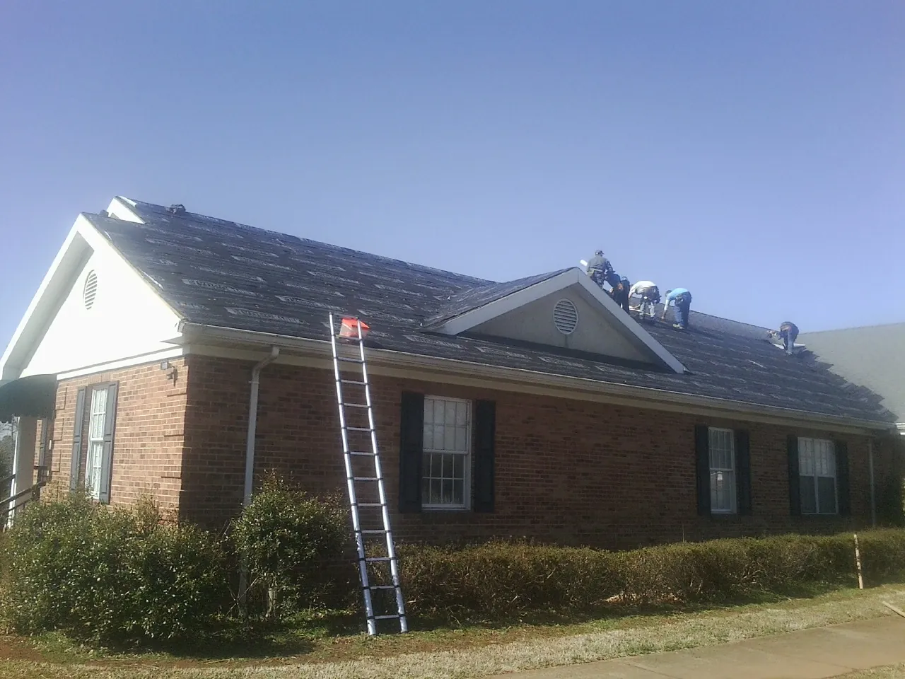 Crew tearing shingles off a brick ranch roof with a ladder set — Metal Roof Repair work by our crew in King