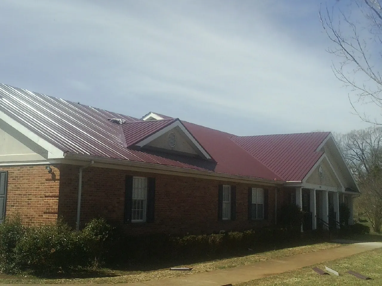 Red metal roof with gabled entries on a long brick building, from a Hail Damage Roof Repair job in King