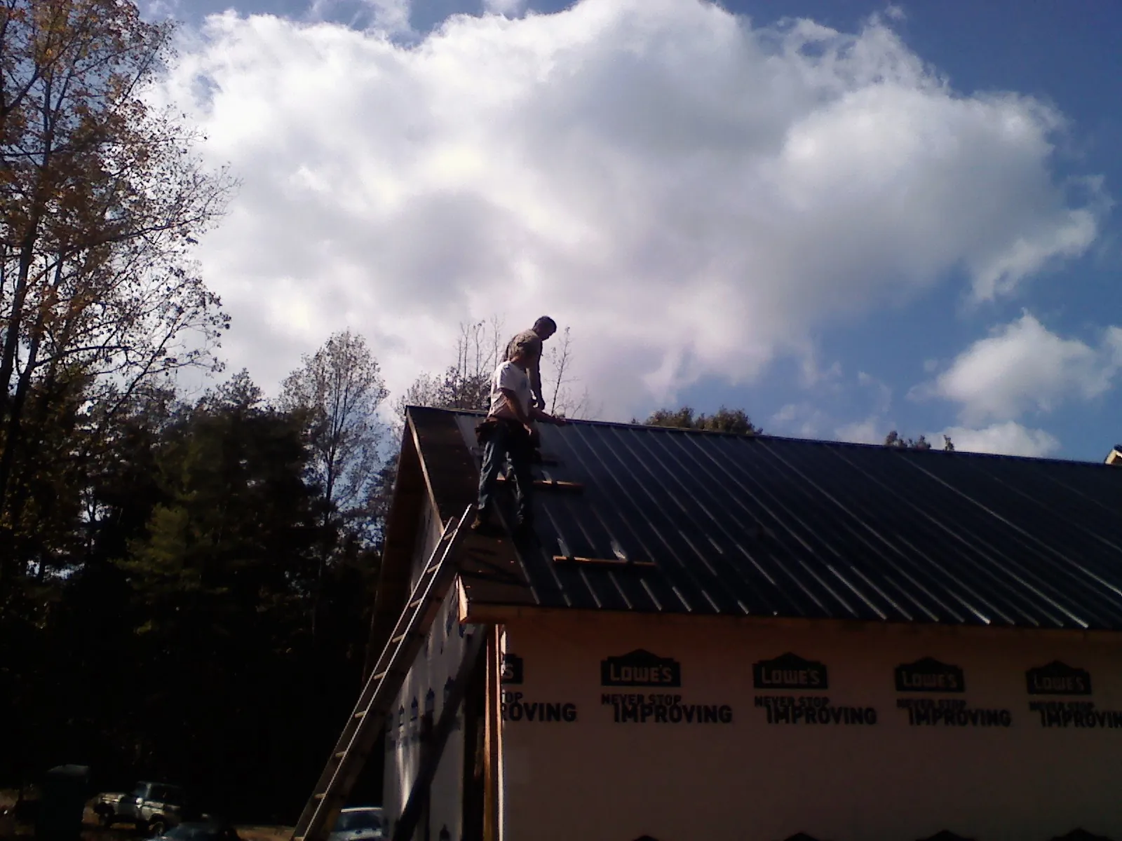 Roofer fastening dark metal panels high against a cloudy sky, from a Roof Inspection job in King